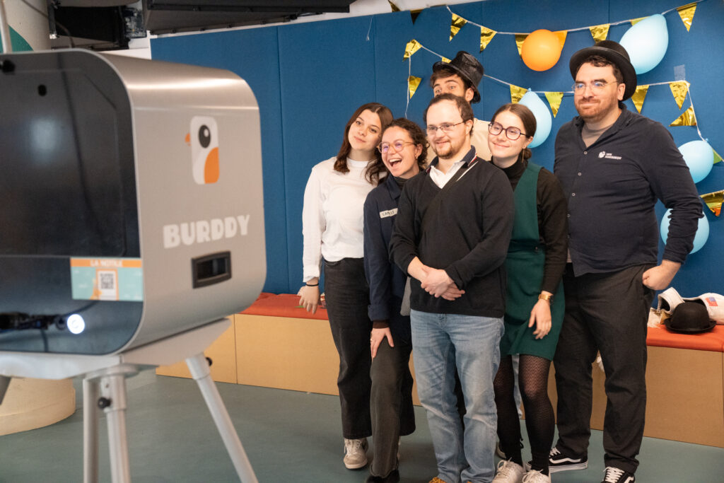 La scène capture un moment festif et détendu où un groupe d'amis ou de collègues prend la pose devant une borne photo automatique (un photobooth).