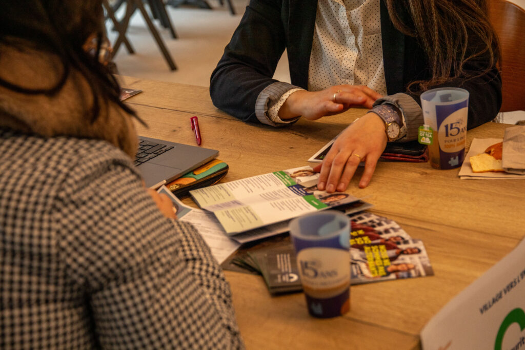 La scène est un plan rapproché et intimiste montrant un échange professionnel en tête-à-tête autour d'une table en bois clair, typique d'un entretien de conseil, d'orientation ou de mentorat.